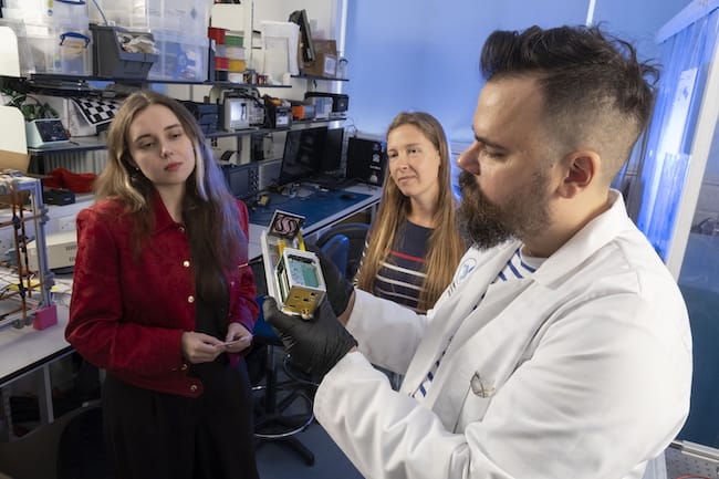 From left: Katie Tubbing, Dr. Keira Tucker, and Dr. Gilles Bailet prepare a bacteria‑dyed fabric prototype at the University of Glasgow’s James Watt School of Engineering ahead of its space mission.