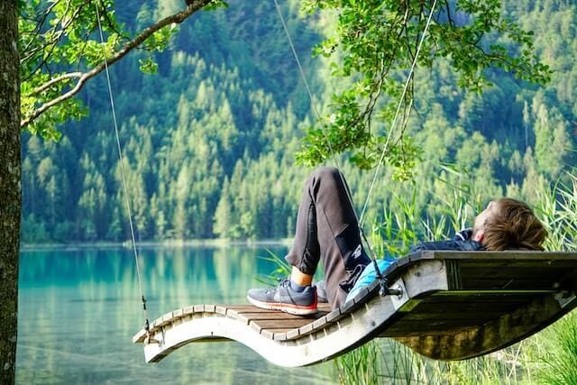 man in black jacket sitting on brown wooden boat on lake during daytime