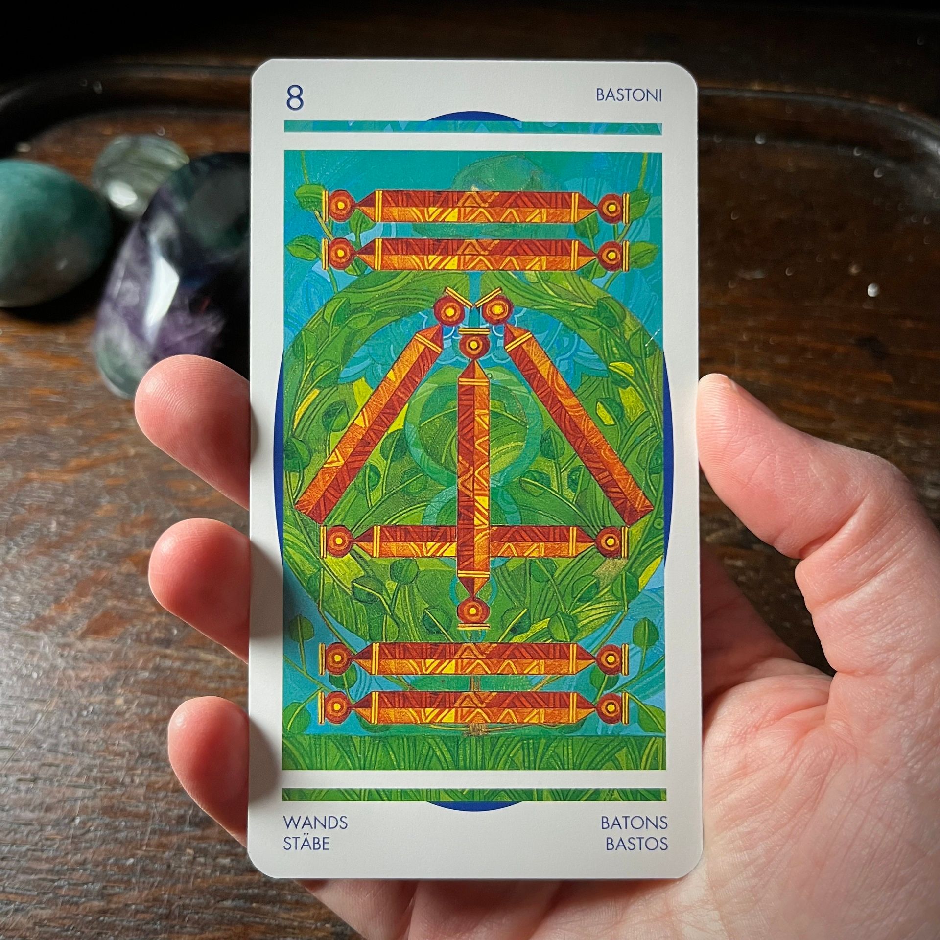 Eight of Wands from the Crystal Tarot shows eight orange wands ona green and blue background