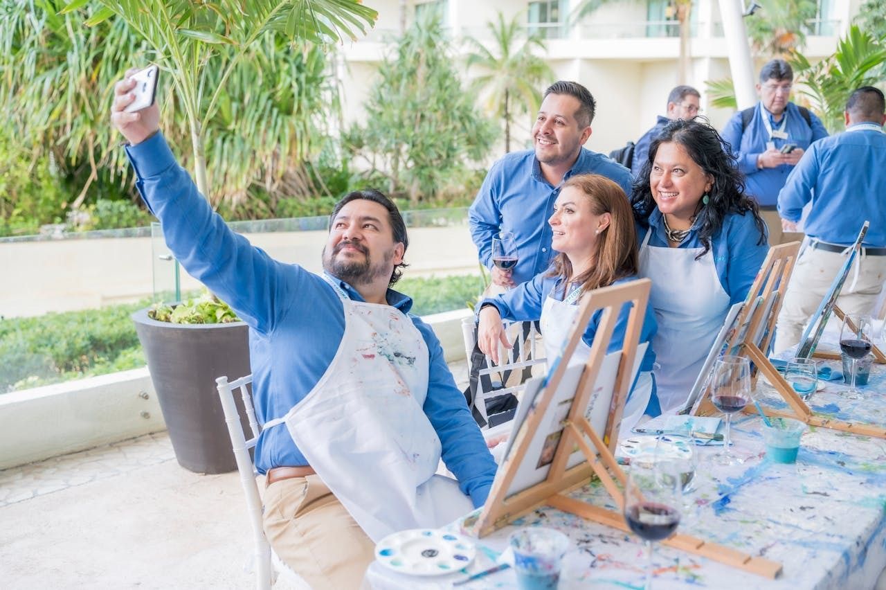 Group of people taking a selfie, in front of a table covered in easels, canvas and paint.