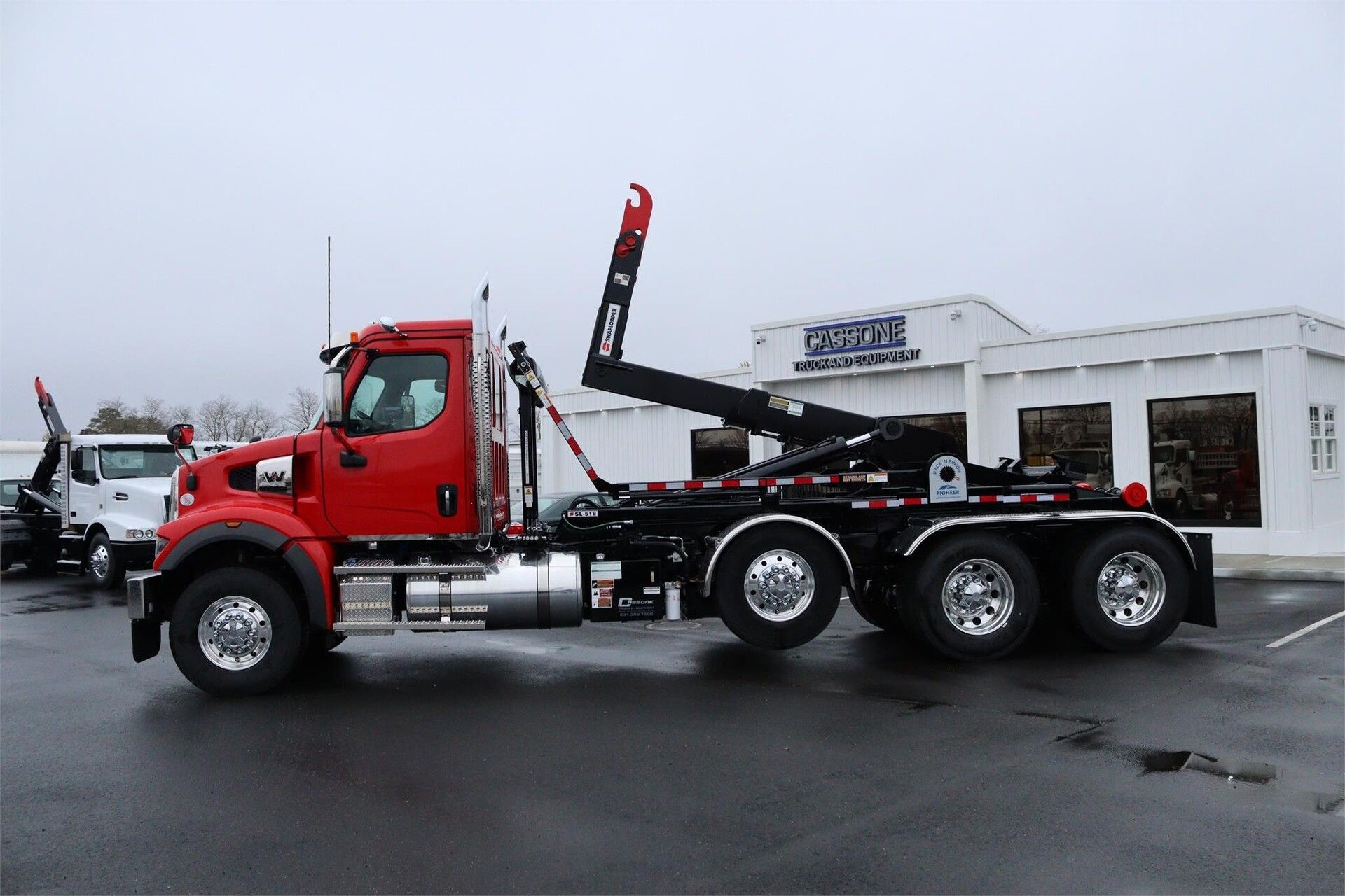 A red Western Star hooklift truck equipped with a SwapLoader system parked at a dealership. Built for heavy hauling, roll-off containers, and municipal fleet use in 2025.