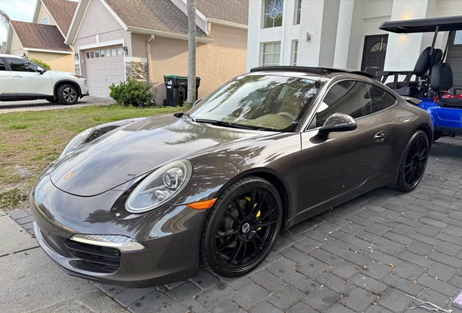 Front three-quarter view of a dark grey 2014 Porsche 911 with black wheels parked on a brick driveway