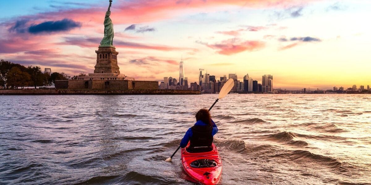 a person kayaking in front of the statue of liberty