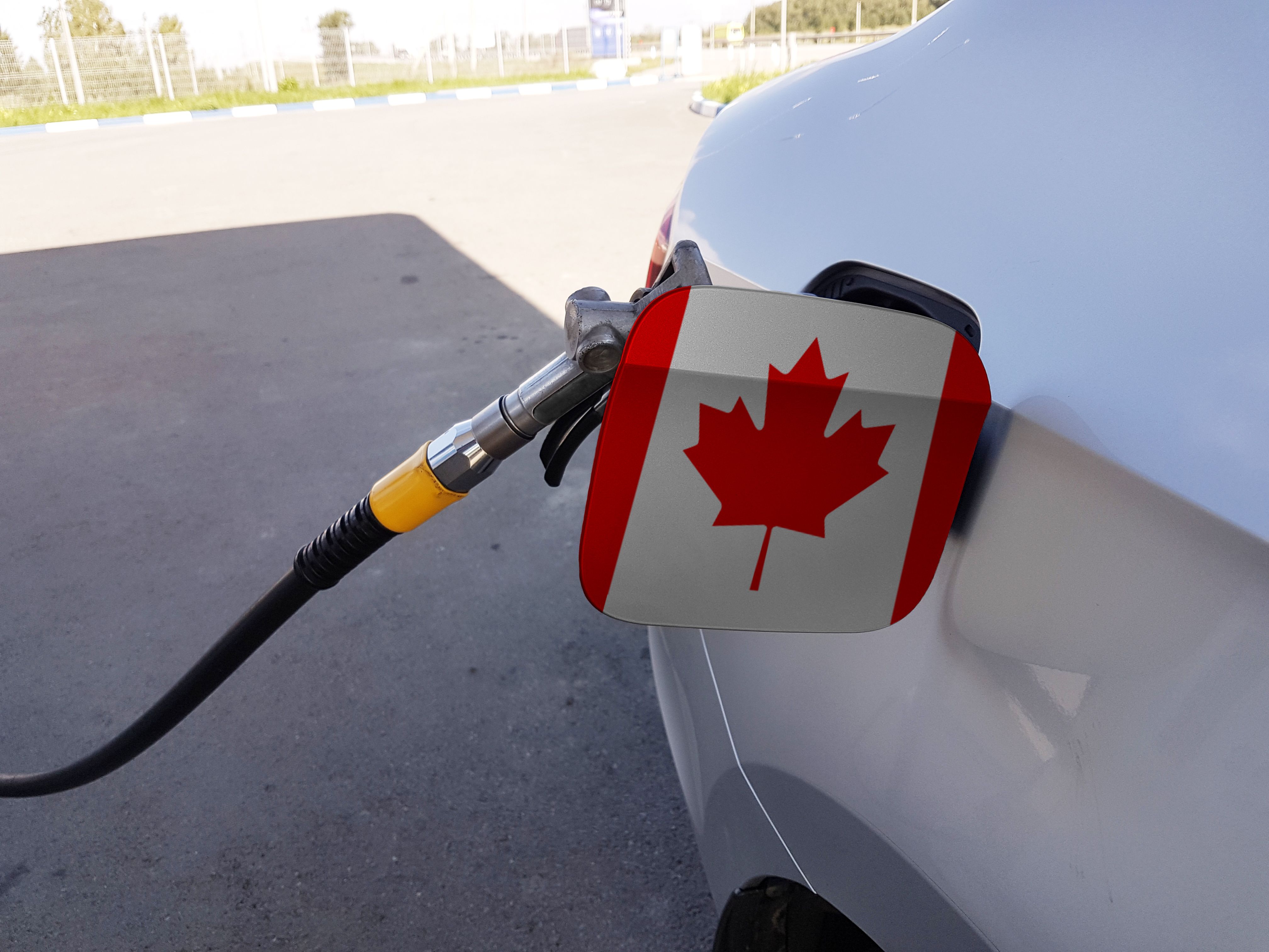 Close-up of a car&rsquo;s fuel cap door with a Canadian flag sticker as the vehicle is being refuelled at a gas station.