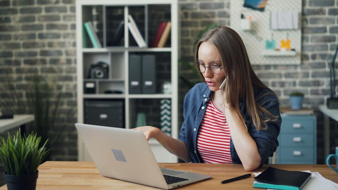 Office worker attractive young woman is arguing on mobile phone with angry face talking gesturing sitting at table. People, business and communication concept.