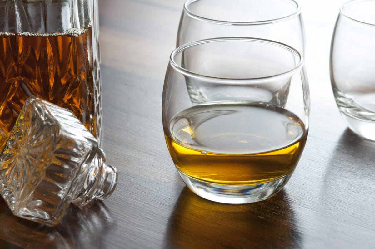 Glass of scotch whiskey alongside an open decanter on a bar counter or table with additional empty glasses