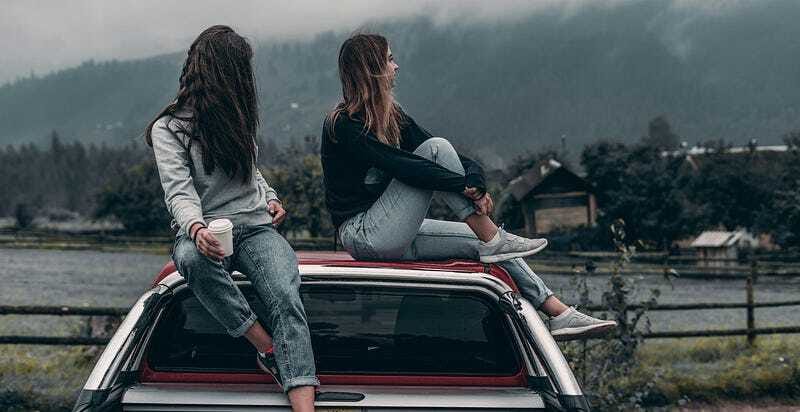 Two young women standing on top of a car under the open sky, celebrating freedom and deep friendship in nature.