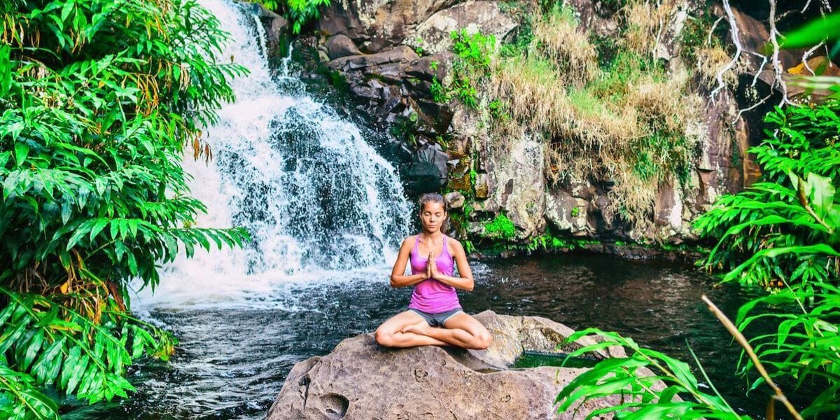 a girl doing a yoga pose on a rock in front of a waterfall