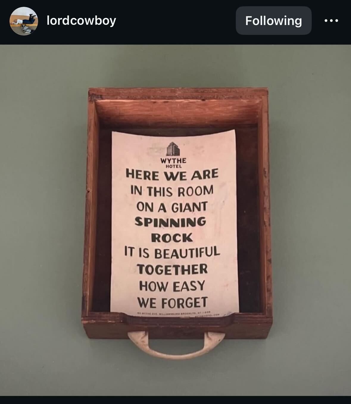 screenshot of an instagram post with an image of a wooden drawer that's been pulled out and laid on a green background. inside the drawer is hotel stationary that says: "WYTHE HOTEL here we are in this room on a giant spinning rock it is beautiful together how easy we forget"