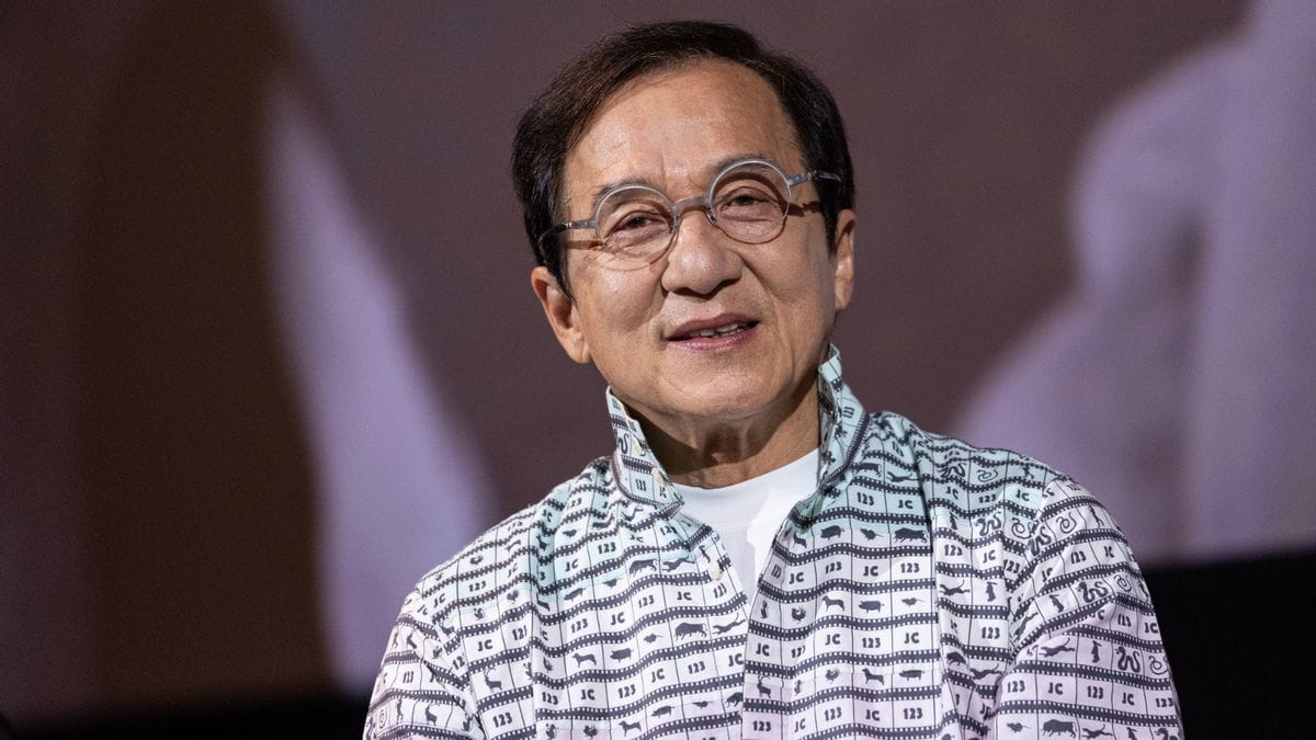 An Asian man wearing glasses speaks while standing on a stage.