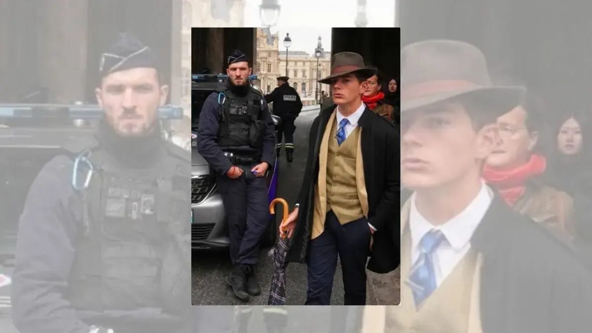 A person wearing a suit and fedora is pictured standing next to a police officer. They're standing outside, and otehr people can be seen in the background.