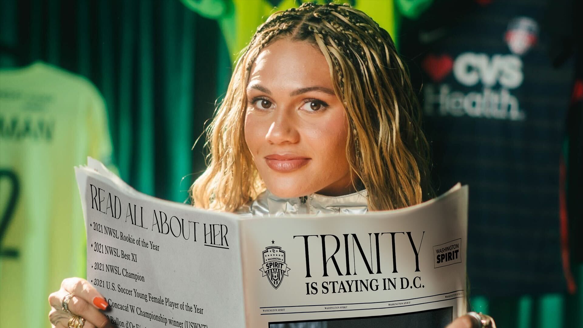 Trinity Rodman poses with a newspaper saying she’s staying in DC against a backdrop of Washington Spirit jerseys.