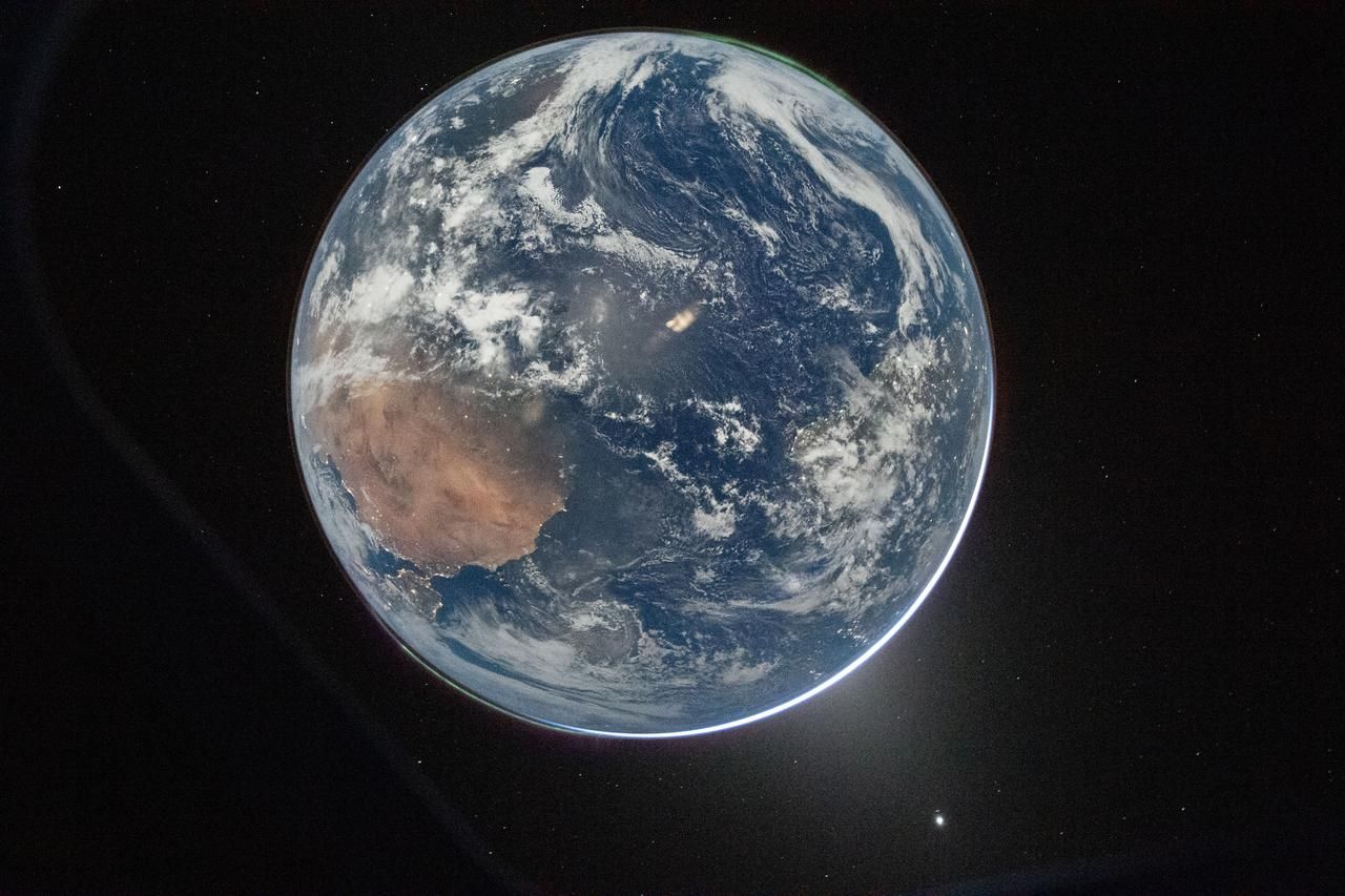A photo of Earth showing northern Africa and the Atlantic Ocean with clouds swirling. Many stars can be seen in the background.