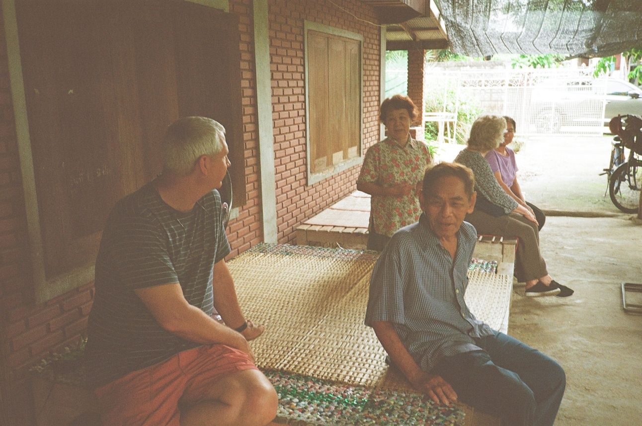 My parents sit on woven mats with friends and chat.
