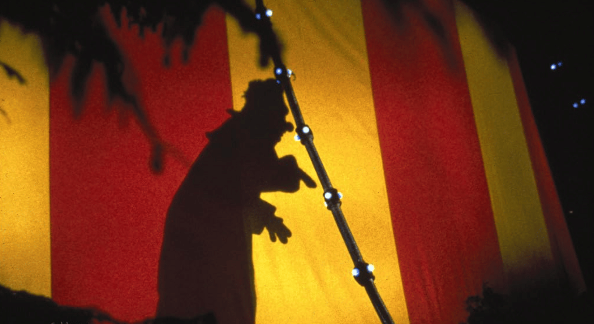 The shadow of a clown is cast in sharp relief on the cloth of a circus tent.