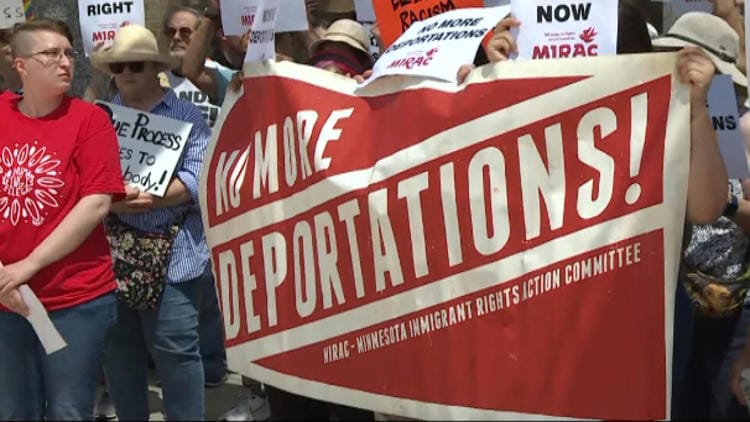 A group of protesters hold a red and white banner that reads, "NO MORE DEPORTATIONS - Minnesota Immigrant Rights Action Committee."