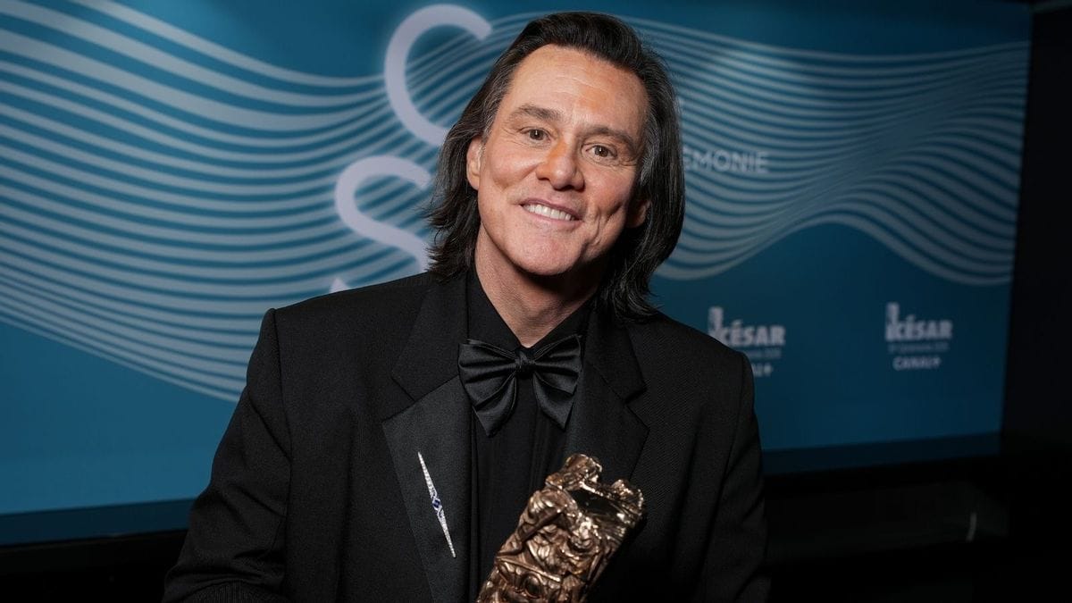 A white man wearing a black suit smiles while holding an award.
