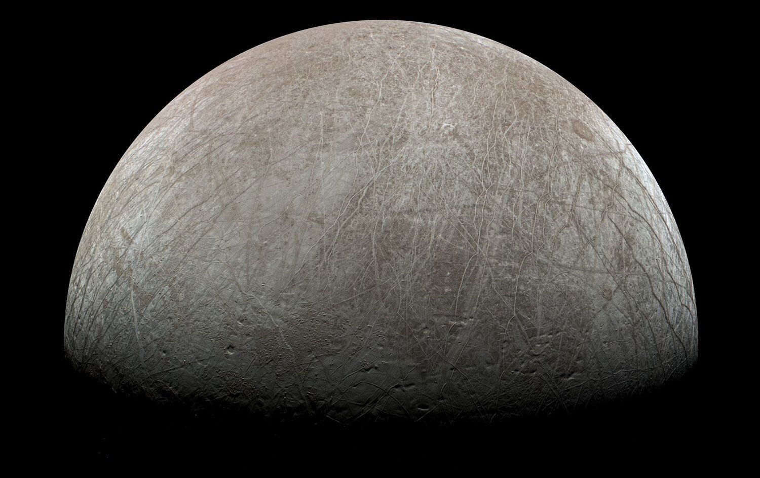 Europa is half lit, a gray-brown moon covered in long cracks.