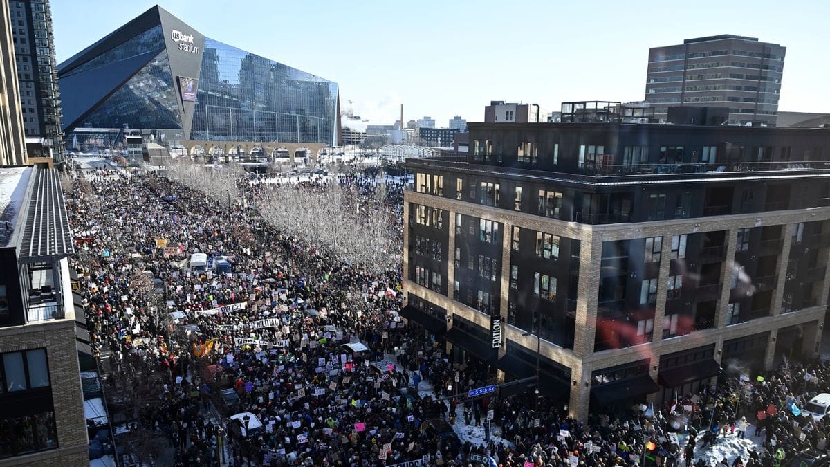 Photo from above of a crowd with anti-ICE protest banners filling a Minneapolis street from one building to the other. The US Bank Center is in the background and the ground is covered in snow