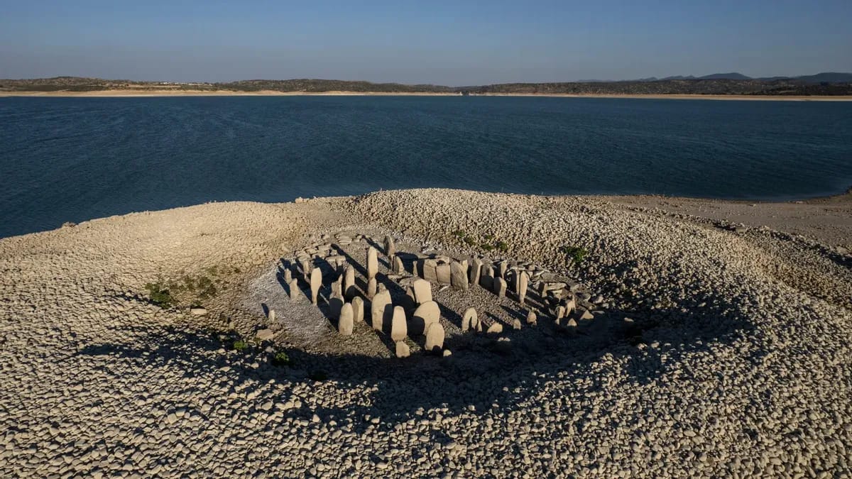 A monument in the sand is shown next to a large body of water.