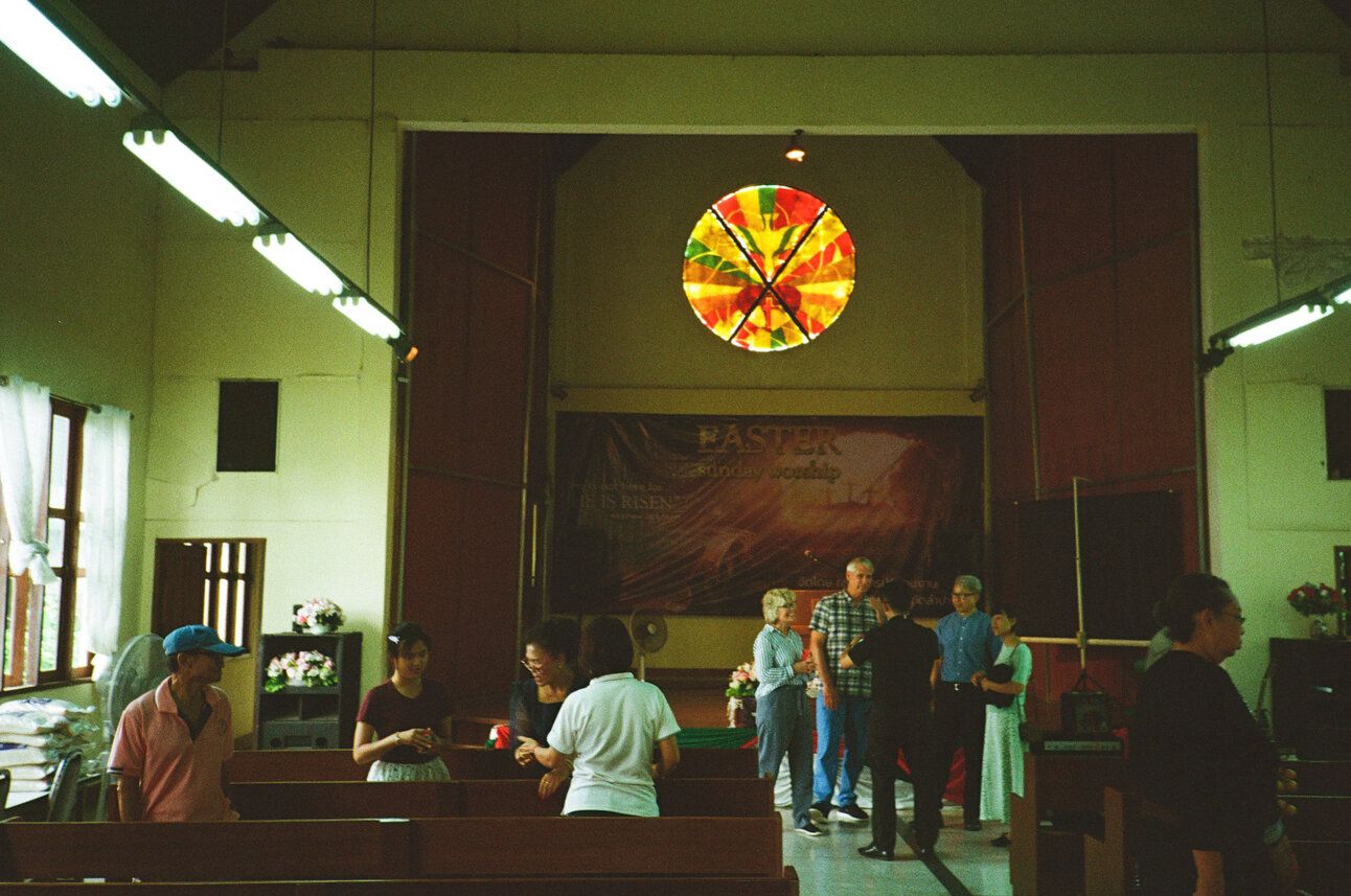 People visit in the pews of the sanctuary of a Thai church.