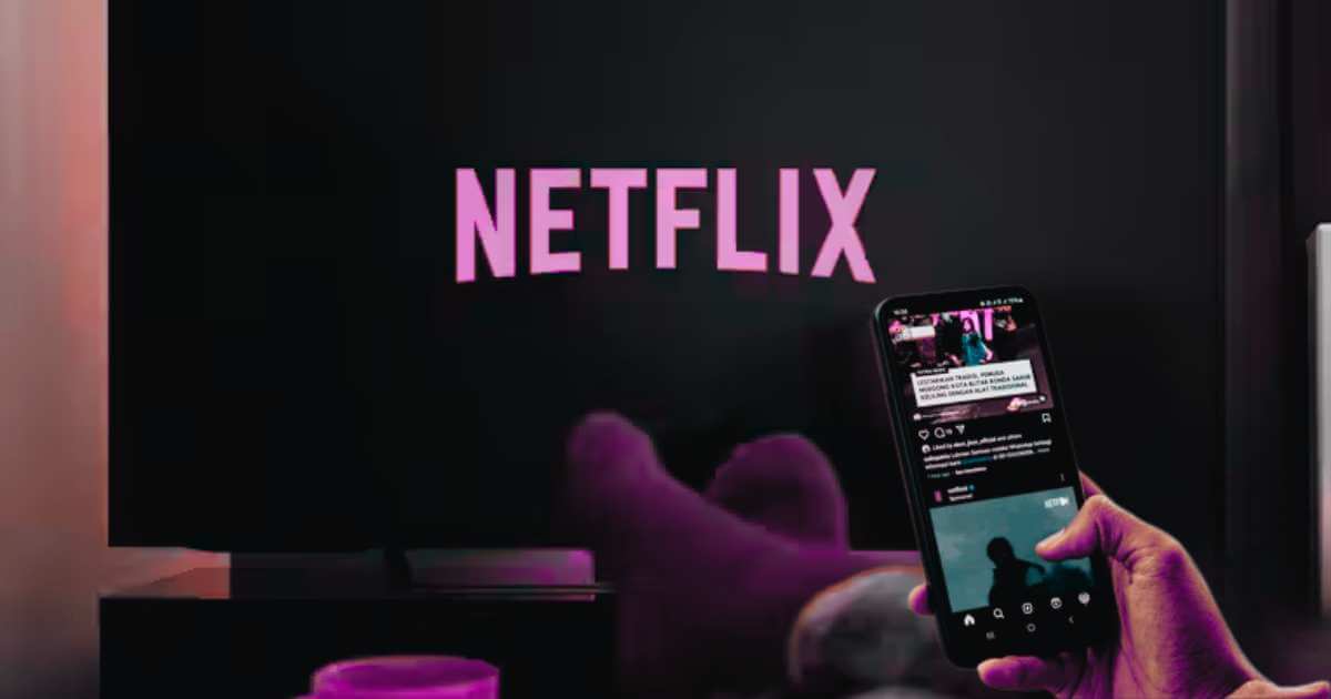 Person scrolling phone while Netflix plays on TV in background - the perfect visual representation of distracted viewing"