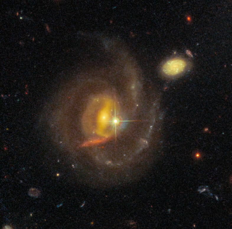 A reddish spiral galaxy with a bright star in it, and a fainter, even redder galaxy behind it.