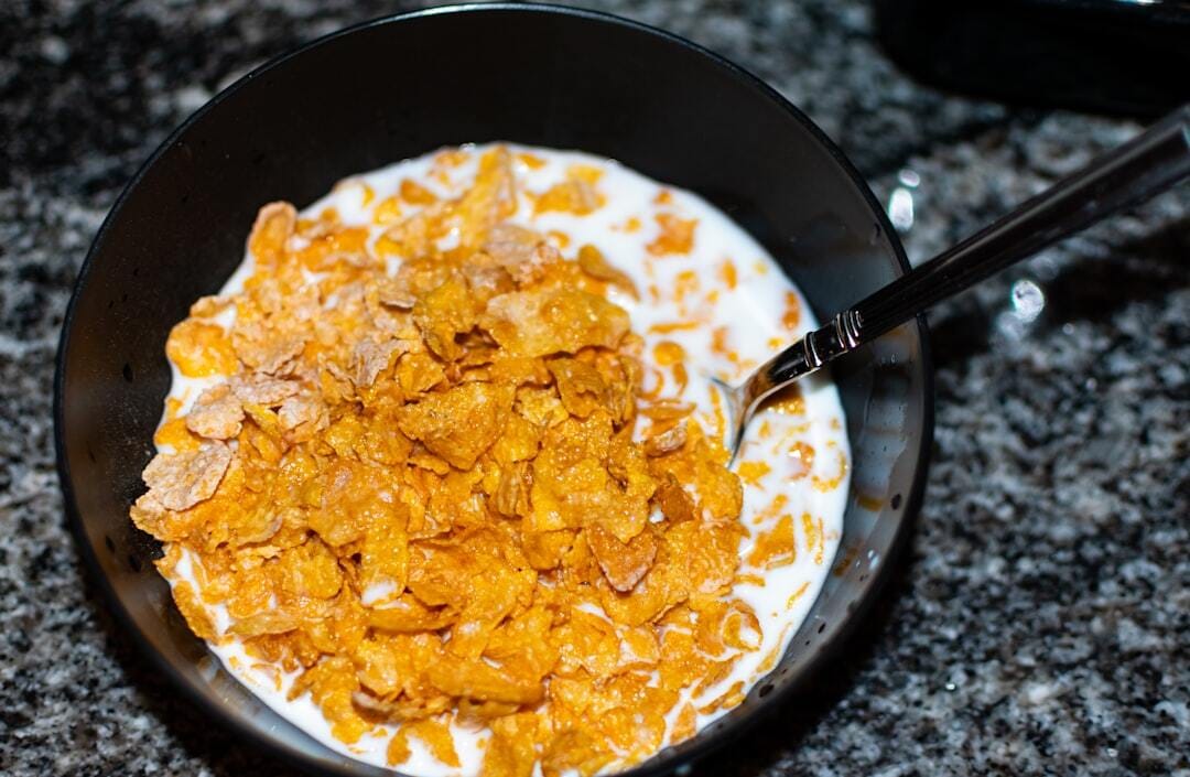 A black bowl of frosted flakes or corn flakes with milk and a spoon.