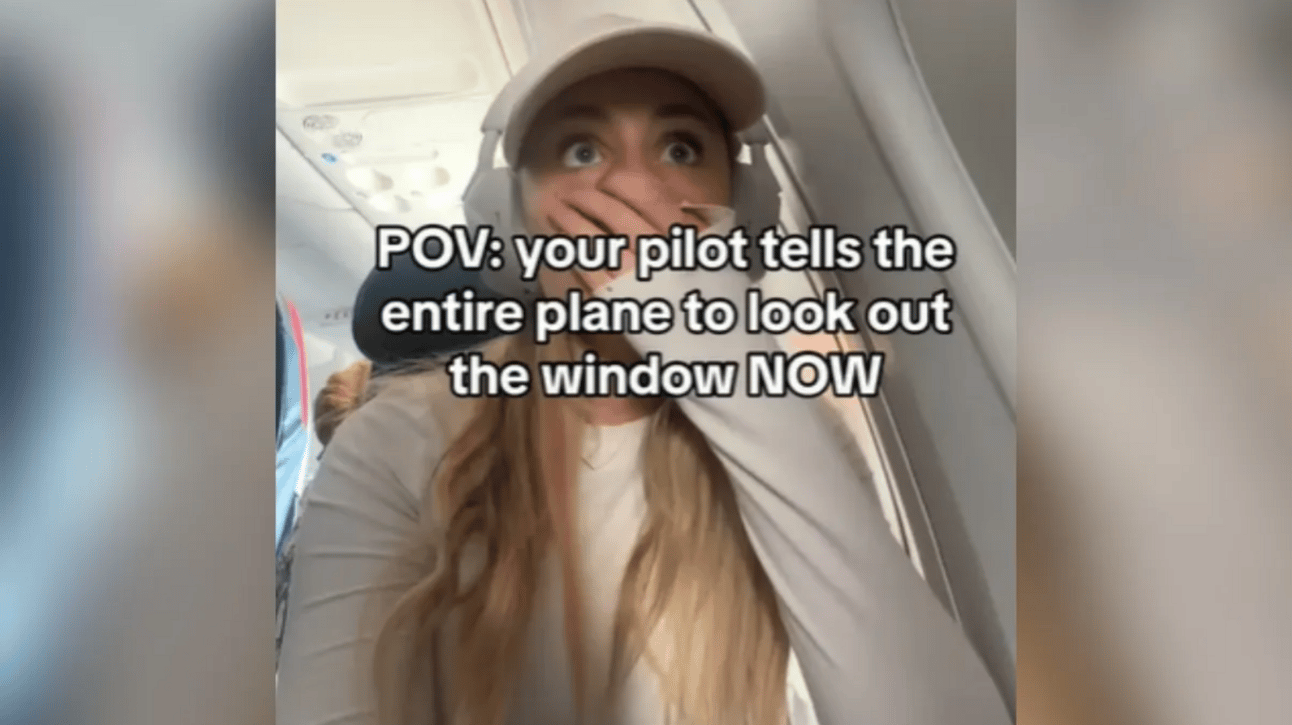A woman sits on a plane, eyes wide as she covers her mouth with her hand. Text on the image reads: POV: your pilot tells the entire plane to look out the window NOW