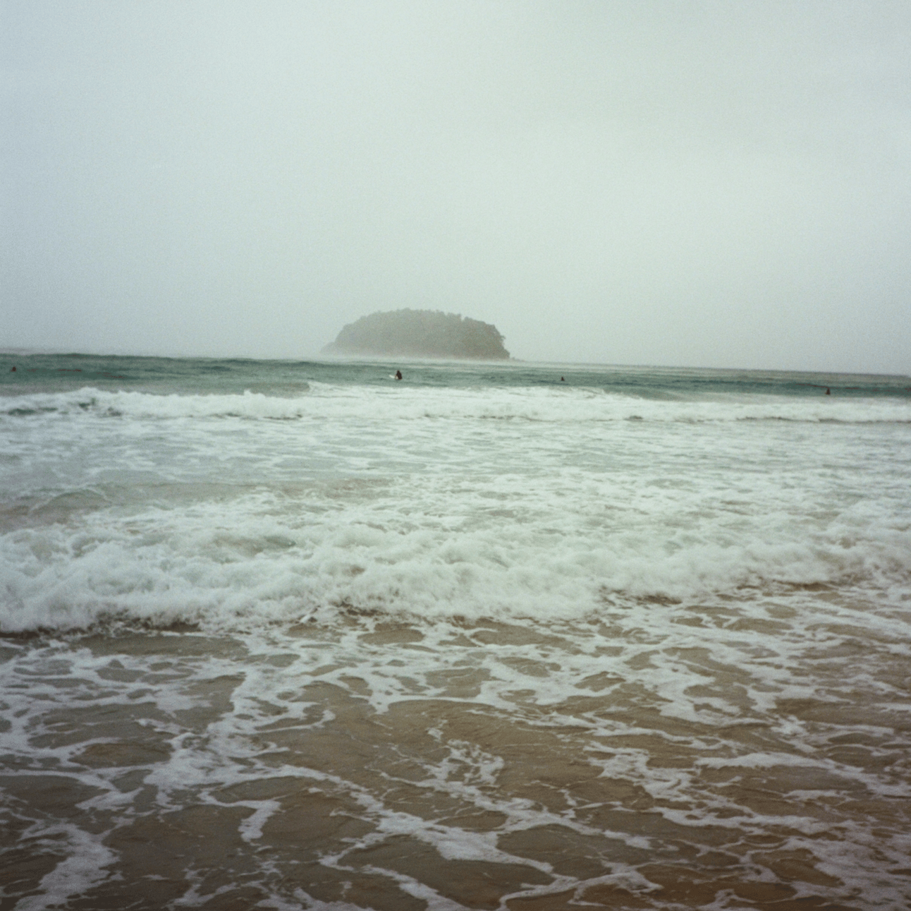 A rainy ocean with a lone surfer in the distance and a fog shrowded island beyond.