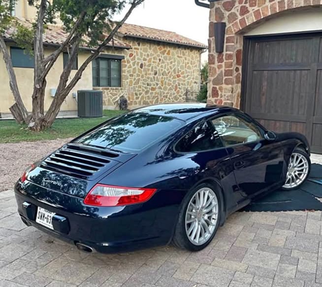 Rear three-quarter view of a dark blue 2006 Porsche 911 parked on a brick driveway in front of a stone house