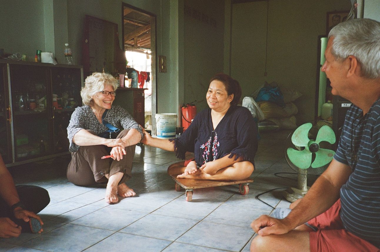 My parents and brother sit on a tile living room floor and visit with a friend.