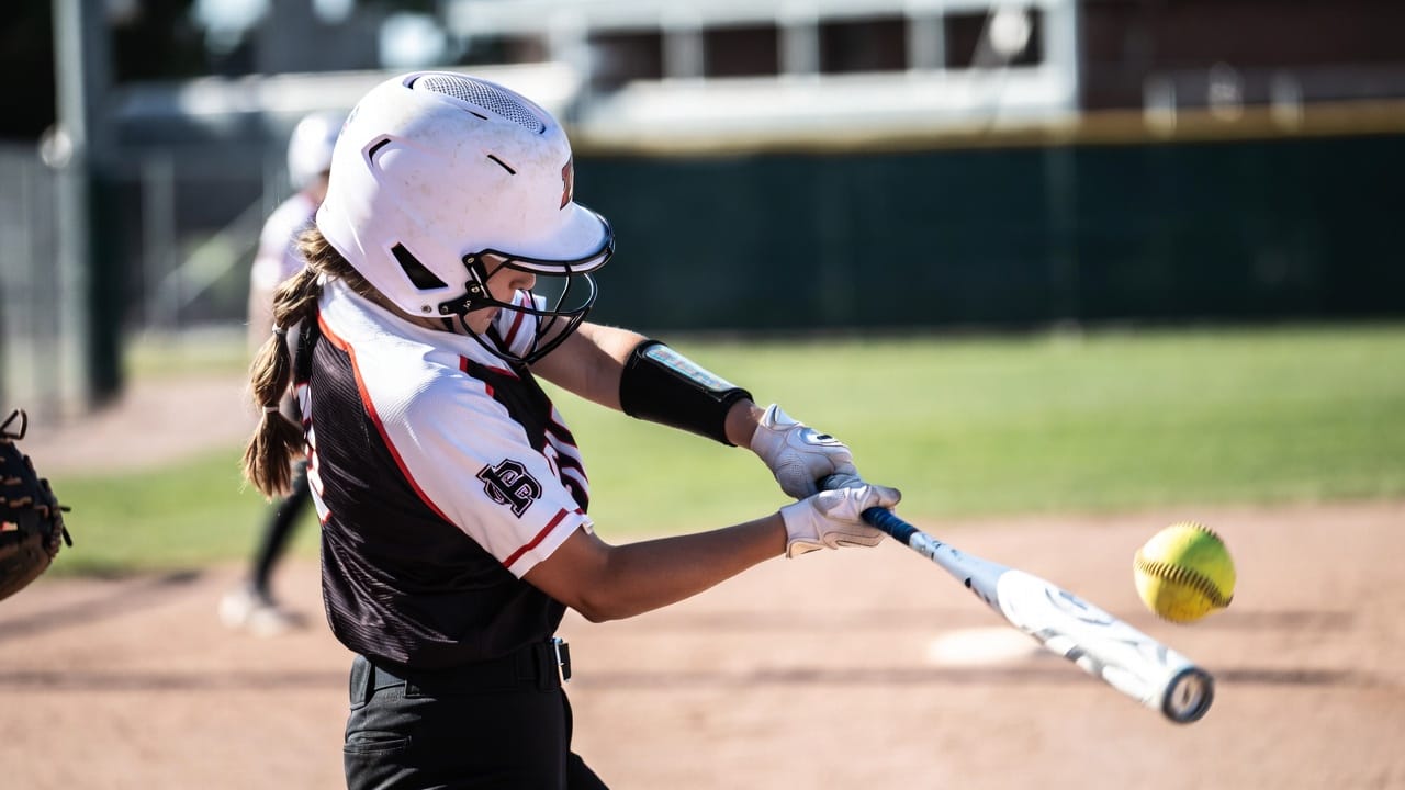 Youth softball player making solid contact during a swing in a game setting
