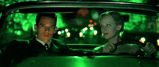 Ethan Hawke sitting in a car with a green background looks at Ume Therman who looks back at him