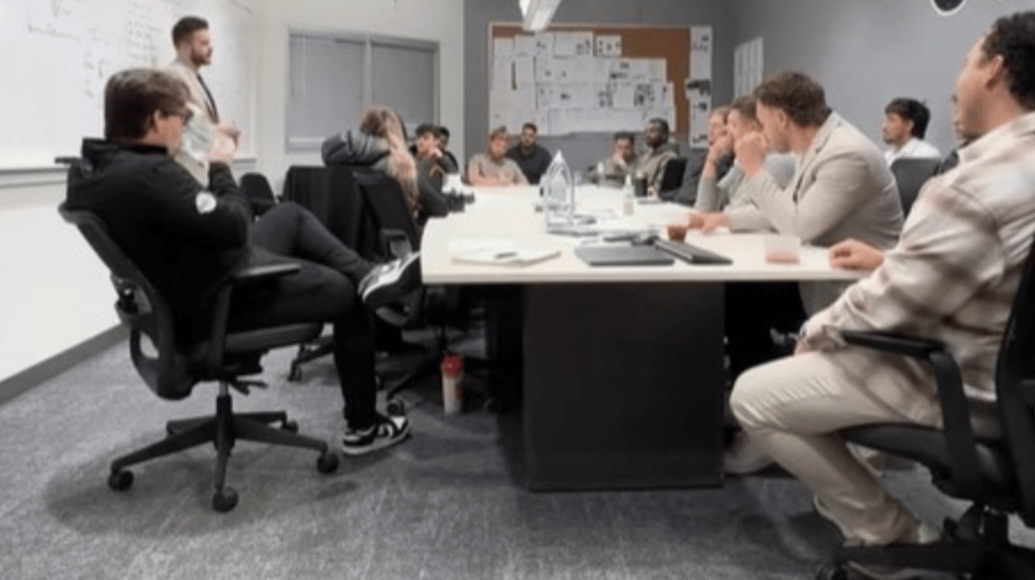Image shows a car salesman training session where the attendees are playing the "anything but a cup" prank on the facilitator.