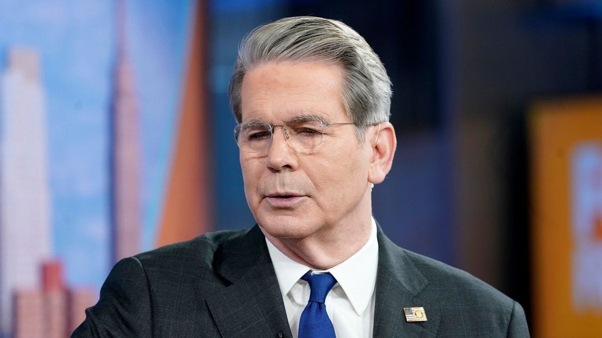 A white man wearing a gray suit appears to speak.