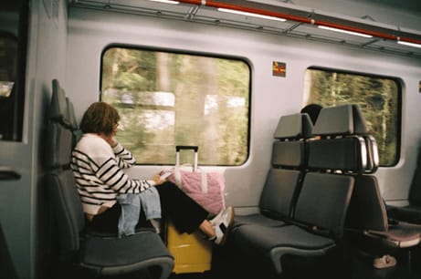 Mujer sentada junto a la ventana en un tren, con maletas a su lado y la vista puesta en el paisaje exterior.