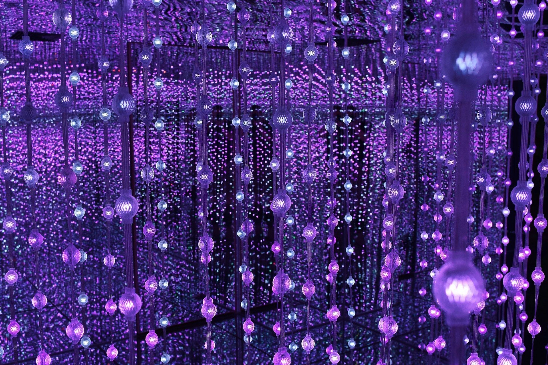 Purple and blue hanging glass or crystal ornaments creating a shimmering curtain effect with reflective surfaces and bokeh lighting in the background