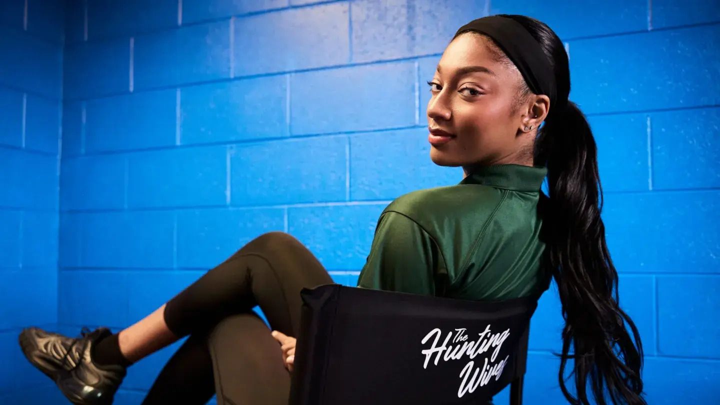 WNBA star Angel Reese poses in a Hunting Wives director’s chair against a blue backdrop.