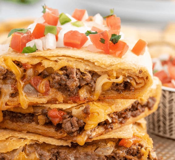 Sheet pan tacos with layers of beef and cheese in taco shells, topped with diced onions and tomatoes