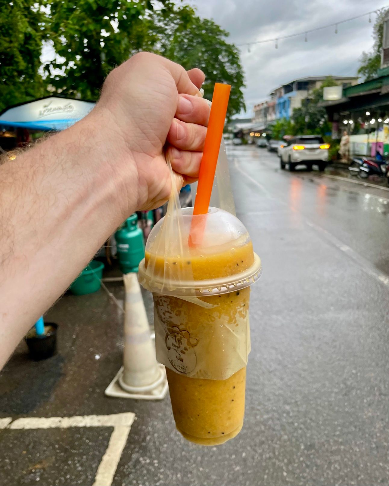 A hand holds a fruit smoothie of mango and passion fruit.
