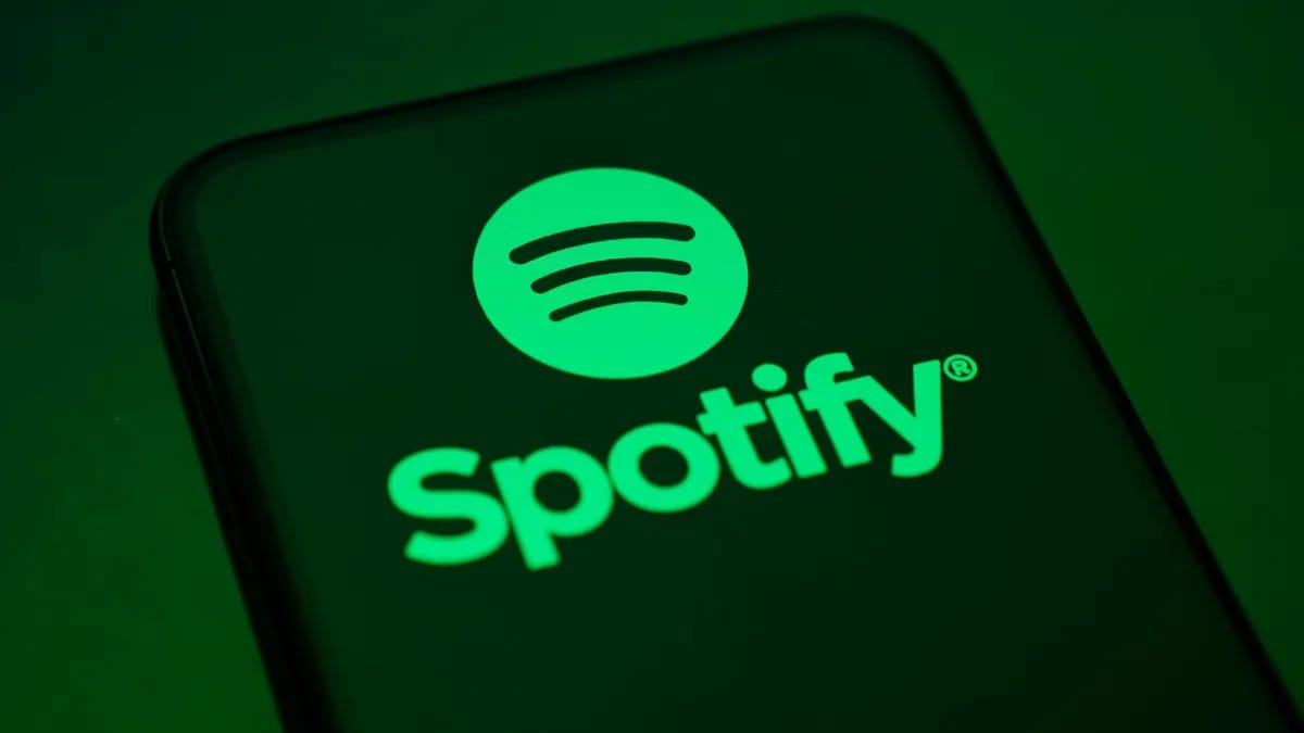 A phone shows a green word that says Spotify below a green circle that has three black lines representing sound waves in there.
