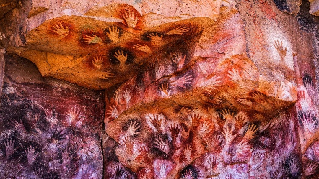 Ancient cave art at Cueva de las Manos in Argentina, showing dozens of hand stencils in red, black, and white pigments across a rock wall.