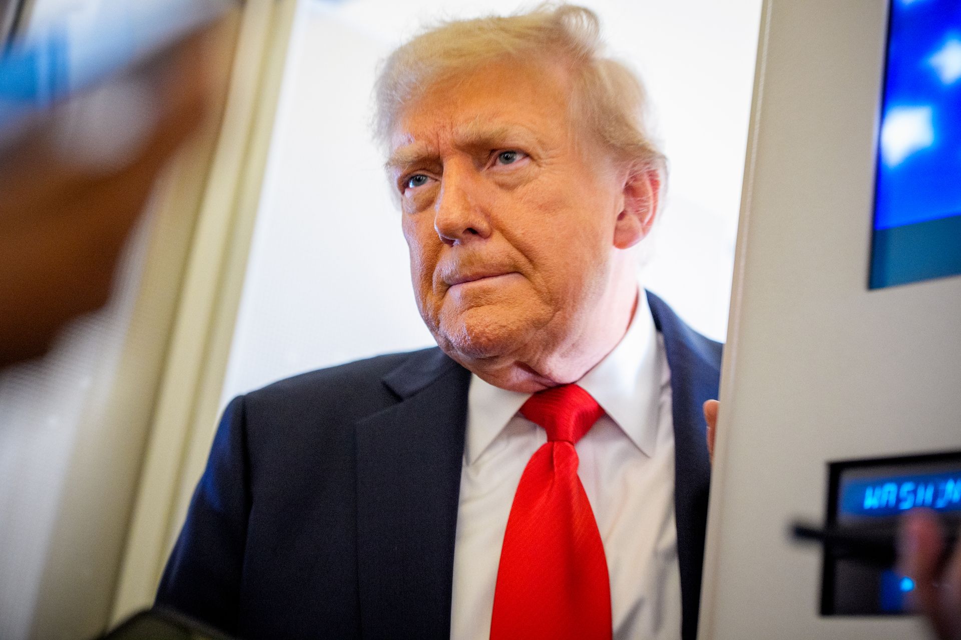 A white man wearing a suit is shown standing in what appears to be a doorway.