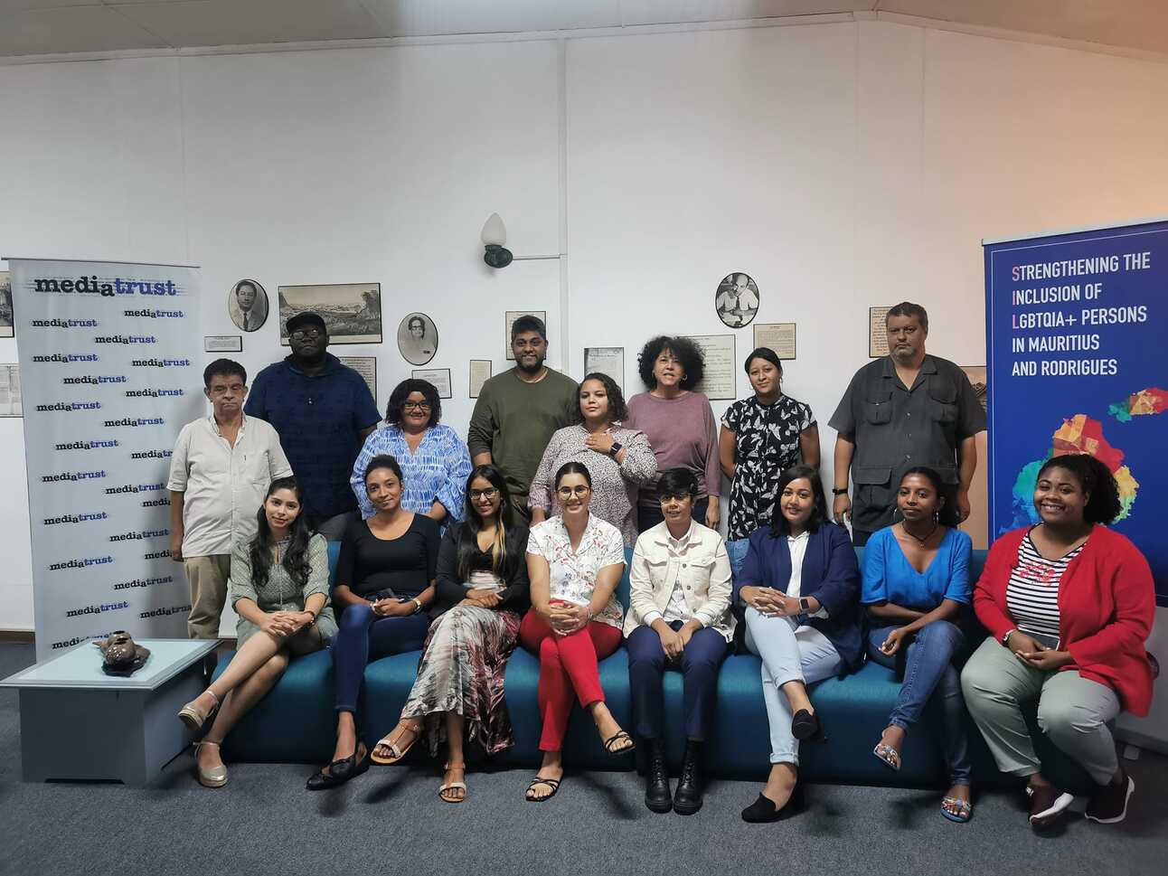 A group of people gathered on a sofa between two banners, one for the media trust an one ofr a queer alliance in Mauritius
