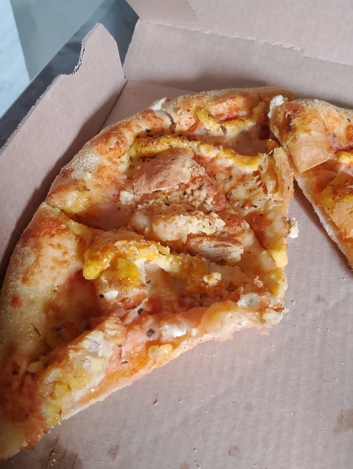Foto de uma caixa d papelão com três edaços de pizza com pão de alho em cima.