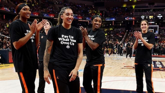 Kiki Iriafen #44 of the Washington Mystics, Gabby Williams #5 of the Seattle Storm, Jackie Young #0 of the Las Vegas Aces, and Sonia Citron #2 of the Washington Mystics wear shirts saying "Pay us what you owe us