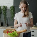 Young Woman With A Bag Of Groceries Checks And Examines A Produc