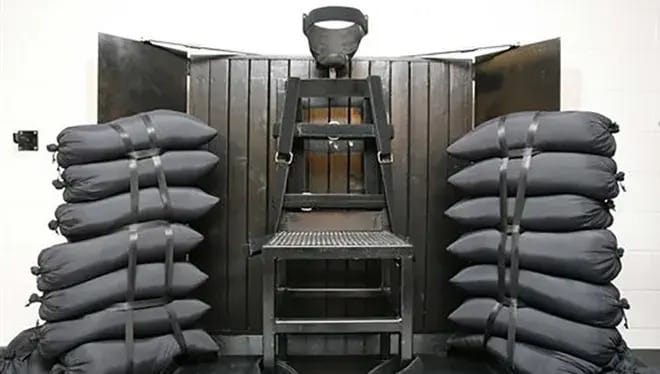 A firing squad chamber, with a chair against a wood backstop, sandbags on either side.