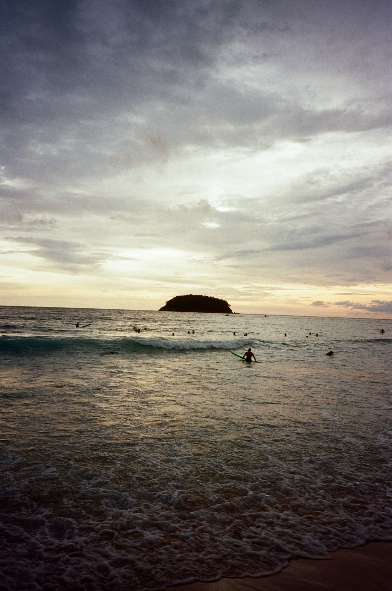 Swimmers and surfers in the ocean at sunset. There's a small island in the distance.